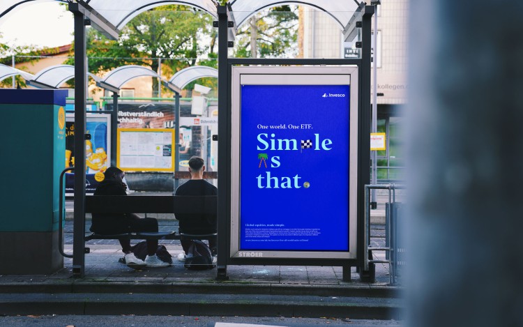 City-Light-Plakat der Invesco-ETF-Kampagne „Simple as that.“ an einer Haltestelle mit wartenden Menschen.
